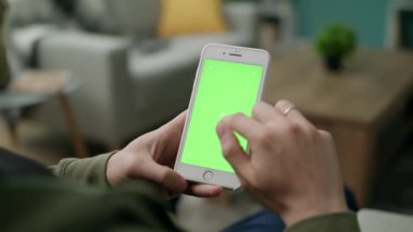 Oturma odasında yeşil ekranlı bir telefon kullanan erkek eller