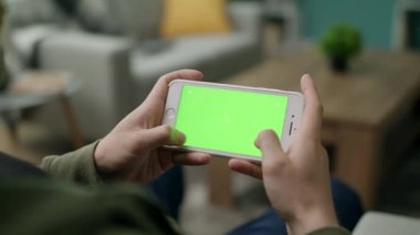 Bir adam oturma odasında yeşil ekran ile bir akıllı telefon üzerinde oynar