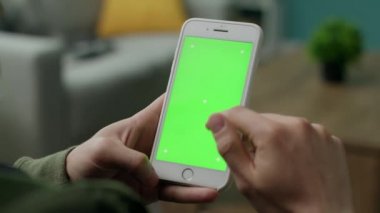 Oturma odasında yeşil ekranlı bir telefon kullanan erkek eller