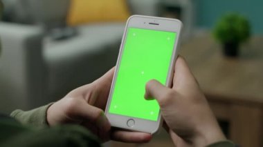 Oturma odasında yeşil ekranlı bir telefon kullanan erkek eller