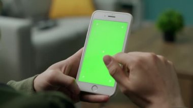 Oturma odasında yeşil ekranlı bir telefon kullanan erkek eller