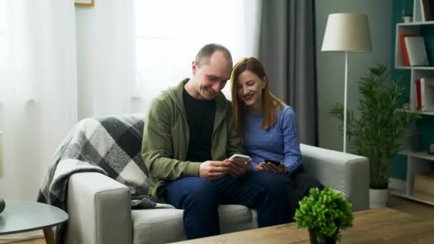 Um jovem casal assistindo a um vídeo divertido em um smartphone em sua acolhedora sala de estar — Vídeo de Stock