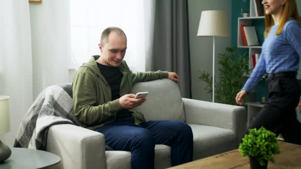 Молодая пара смотрит забавное видео на смартфоне в своей уютной гостиной — стоковое видео