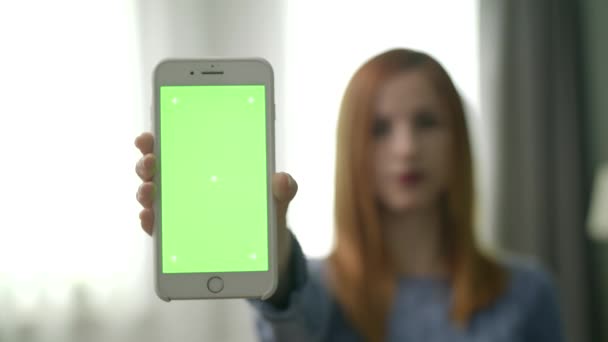 Mujer bastante joven en la habitación muestra teléfono inteligente con pantalla verde — Vídeos de Stock