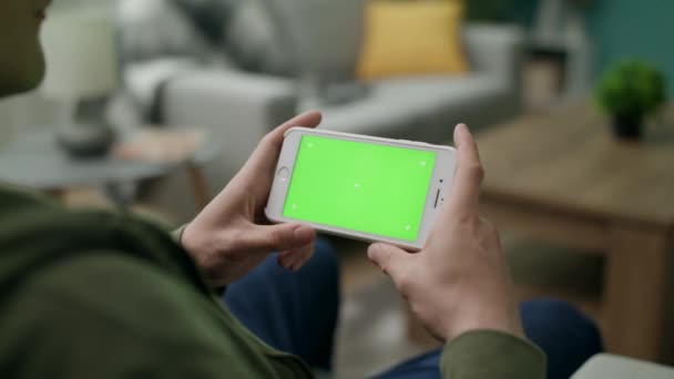 En man tittar på en video på en grön skärm i vardagsrummet — Stockvideo