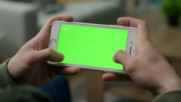 Un hombre juega en un smartphone con una pantalla verde en la sala de estar — Vídeo de stock