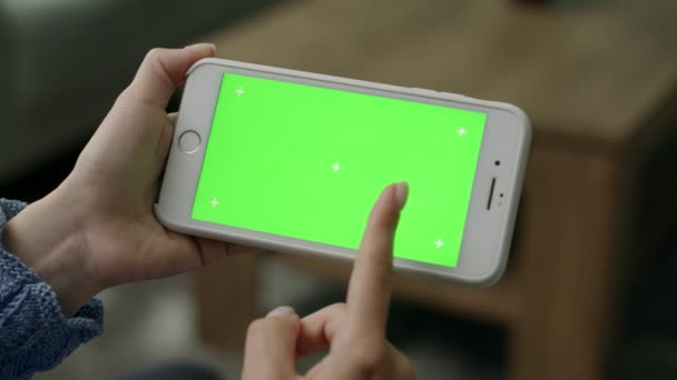 Жінка вдома сидить на дивані, використовуючи зелений макет екрану смартфона — стокове відео