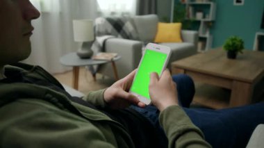 Yeşil Mock-up Ekran ile Smartphone kullanarak Bir Kanepede Evde Man Sitng