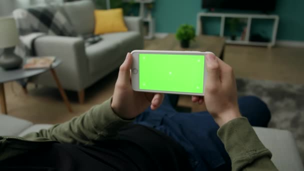 Man thuis Sitng op een bank met behulp van smartphone met groen mock-up scherm — Stockvideo