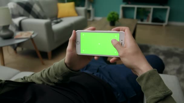 Man hemma Sitng på en soffa med smartphone med grön mock-up skärm — Stockvideo