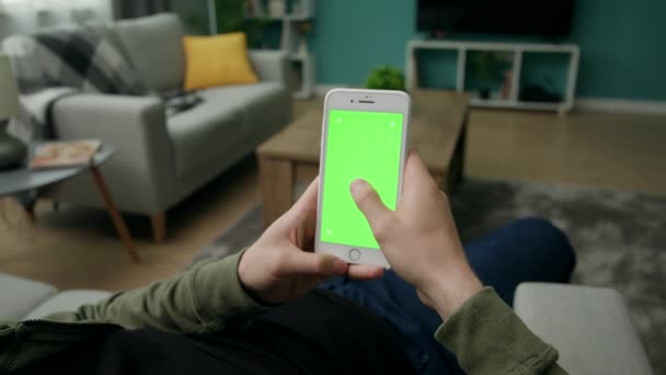 Hombre en casa Sitng en un sofá usando Smartphone con pantalla verde Mock-up — Vídeo de stock
