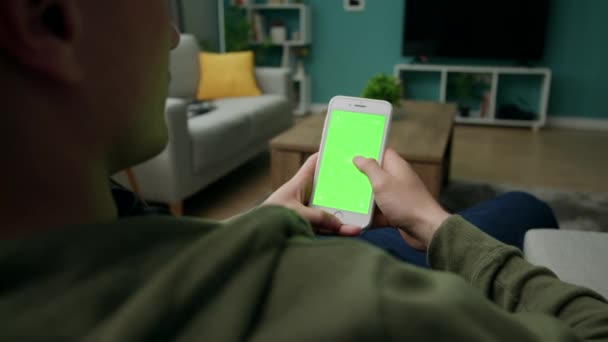 Man hemma Sitng på en soffa med smartphone med grön mock-up skärm — Stockvideo