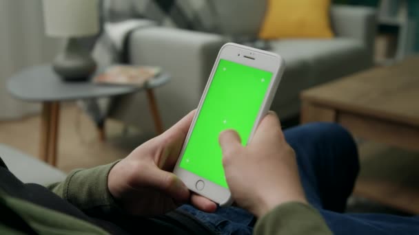 Homme à la maison assis sur un canapé à l'aide d'un téléphone intelligent avec écran vert maquillé — Video