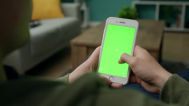 Hombre en casa Sitng en un sofá usando Smartphone con pantalla verde Mock-up — Vídeo de stock