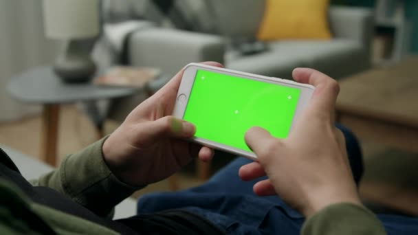 Homem em casa Sitng em um sofá usando Smartphone com tela de Mock-up verde — Vídeo de Stock