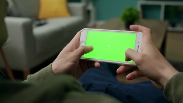 Homme à la maison assis sur un canapé à l'aide d'un téléphone intelligent avec écran vert maquillé 