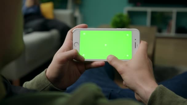 Man hemma Sitng på en soffa med smartphone med grön mock-up skärm — Stockvideo