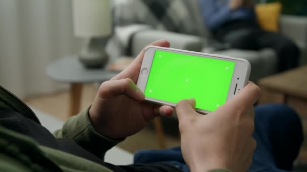 Man thuis Sitng op een bank met behulp van smartphone met groen mock-up scherm — Stockvideo