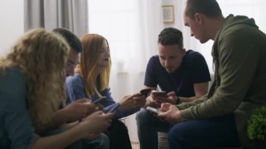 Telefon larını kullanan mutlu arkadaşlar grubu kanepede oturup kapalı alanda oturup eğlenerek konuşurken gülüyorlar.