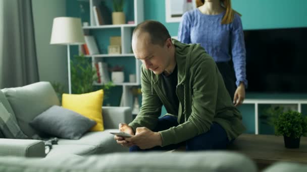 Meisje knuffelen achter de man die zit op de Bank met de telefoon — Stockvideo