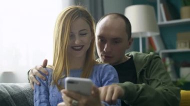 Oturma odasındaki kanepede akıllı telefon kullanan bir çift.