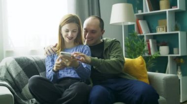 Oturma odasındaki kanepede akıllı telefon kullanan bir çift.
