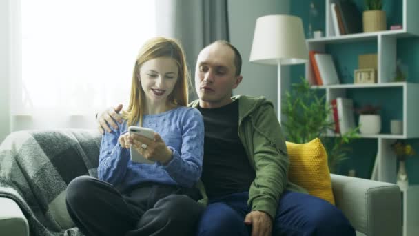 Egy pár együtt használ egy okostelefon a kanapén a nappaliban — Stock videók