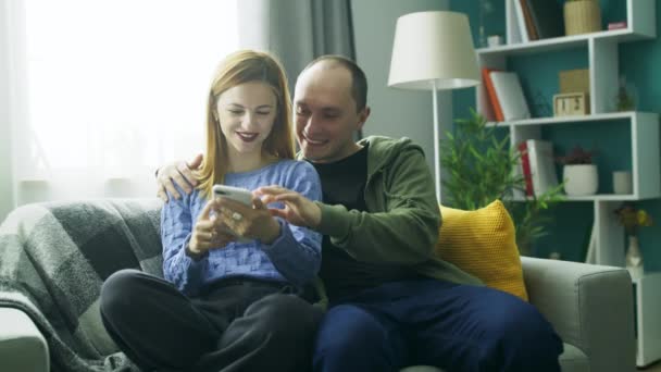 Una pareja usando un teléfono inteligente en el sofá de su sala de estar — Vídeo de stock