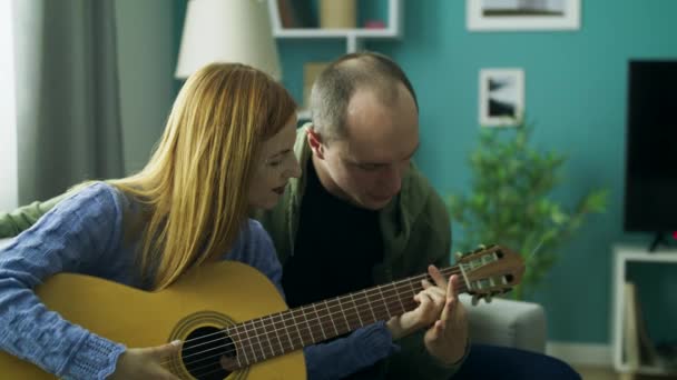 El chico enseña a chica a tocar la guitarra en su sala de estar — Vídeo de stock