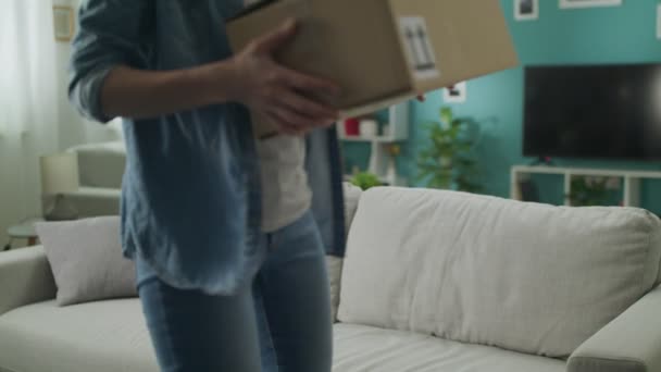 Jonge vrouw betreedt zijn woonkamer met kartonnen doos pakket en het openen ervan — Stockvideo