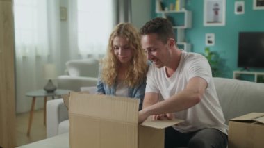 Mutlu çift oturma odasında kanepede oturan açık açma karton kutu koli açma