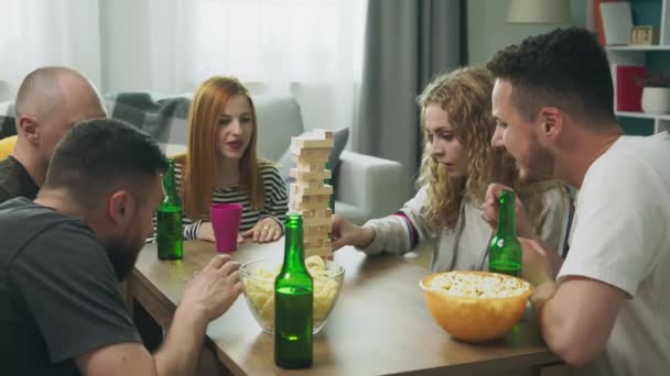 Una compañía de amigos juega una torre de madera en un acogedor salón — Vídeo de stock