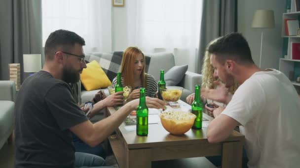 Gezelschap van jongens en meisjes spelen bordspel in de woonkamer en het drinken van bier — Stockvideo