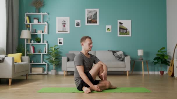 Dolly en de hombre joven haciendo yoga en la mañana en su sala de estar — Vídeo de stock