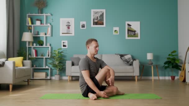 Dolly in von jungem Mann, der morgens Yoga in seinem Wohnzimmer macht — Stockvideo