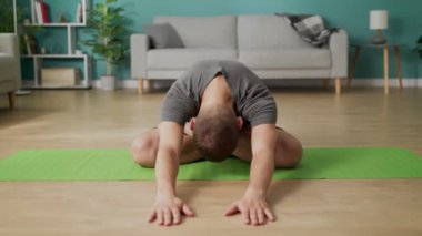 Genç adam sabah yoga yapıyor. Oturma odasında.