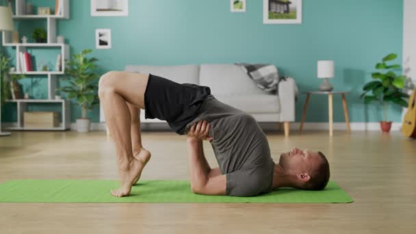 Молодий чоловік робить йогу вранці у своїй вітальні — стокове відео
