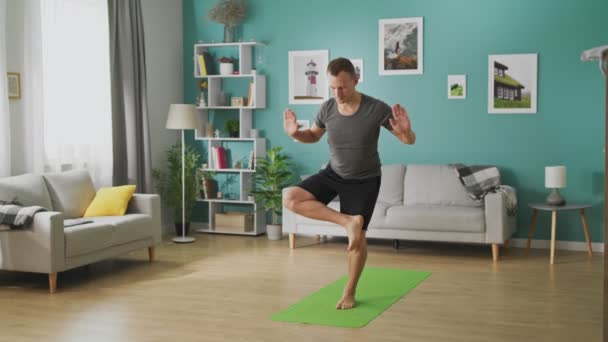 Młody człowiek uprawia jogę rano w swoim salonie — Wideo stockowe