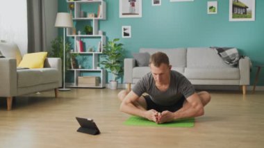 Genç adam tabletteki talimatlara uyuyor ve Asana dansı yapıyor.