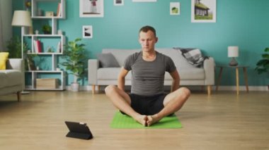 Genç adam tabletteki talimatlara uyuyor ve Asana dansı yapıyor.