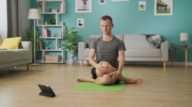 Genç bir adam bir tablet üzerinde talimatları kullanarak yoga çalışmaları