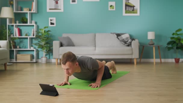 Молодой человек изучает йогу, используя инструкции на планшете. — стоковое видео