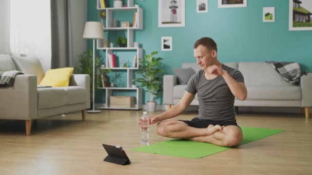 Hombre bebiendo agua de una botella durante clases de yoga en línea — Vídeos de Stock