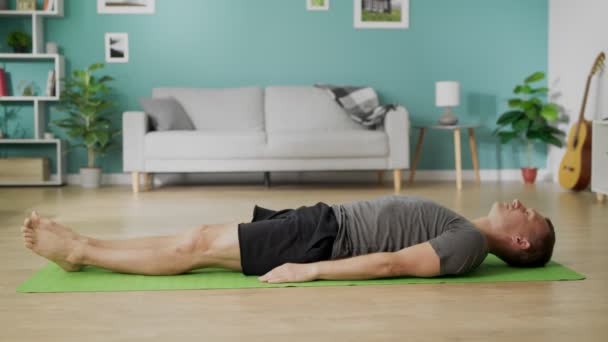 El hombre está haciendo yoga en casa por la mañana en su sala de estar — Vídeos de Stock