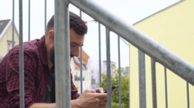 Adam yangın merdiveninde telefonla oturuyor.