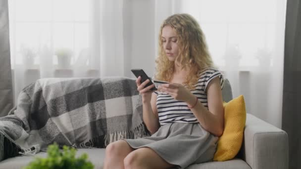 Menina faz compras por telefone celular em casa no sofá — Vídeo de Stock