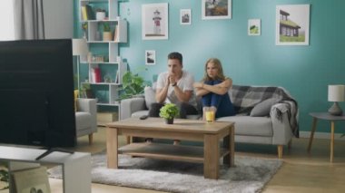 Genç çift rahat bir oturma odasında kanepede TV 'de korkutucu bir film izliyor
