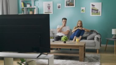 Genç çift rahat bir oturma odasında kanepede TV 'de korkutucu bir film izliyor