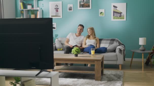 Happy jong stel TV kijken op de Bank in een gezellige woonkamer — Stockvideo