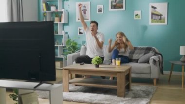 Genç çift rahat bir oturma odasında bir kanepede televizyonda futbol izliyor
